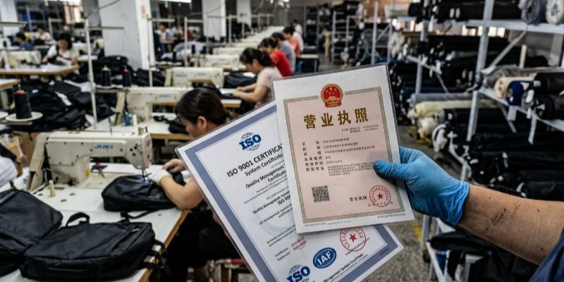 Inspector holding legitimate Chinese business license and ISO certification in a working bag factory
