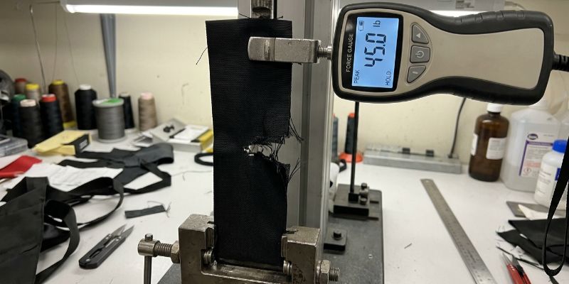 Digital force gauge pulling bag fabric to a 45 lb tear limit in a factory lab